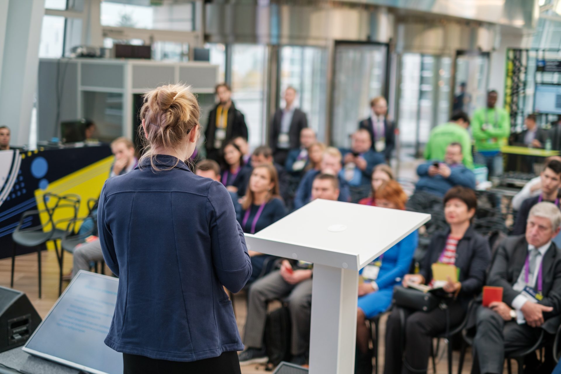 une femme parle de dos devant une assemblée de personnes