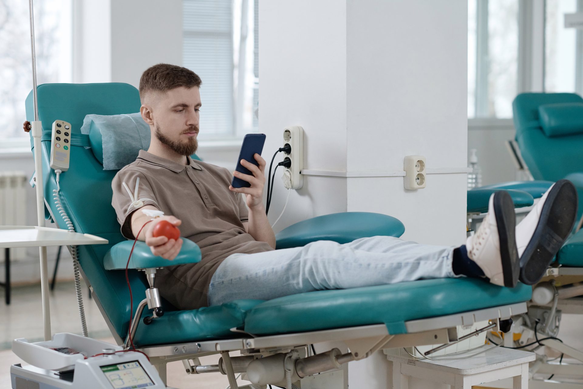 un jeune homme donne son plasma en regardant son téléphone